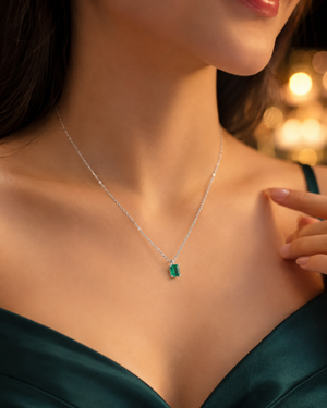 Woman wearing natural emerald solitaire pendant with white gold chain for elegant evening styling 