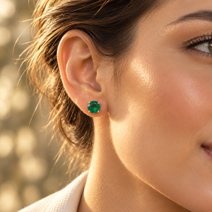 Emerald studs worn on the ear in an elegant setting as May birthstone earrings 