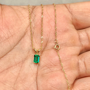 14K yellow gold emerald solitaire pendant with a 6x4 mm medium-dark green lab emerald, smooth prong setting, shown at true-to-life scale. 
