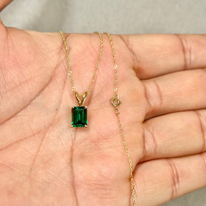Close view of 8x6 mm AAA Russian Lab Created Emerald in 14K yellow gold solitaire pendant on an 18-inch Singapore chain, showing rich green hue and polished prong setting. 