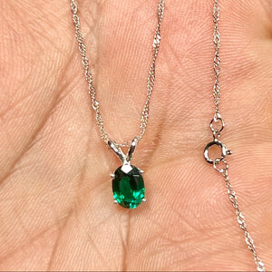 Oval green lab emerald solitaire in polished 14K white gold, four-prong set on a fine Singapore chain, shown at true pendant scale. 