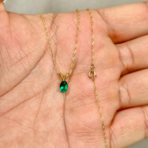 Oval emerald solitaire pendant in 14K yellow gold showing smooth polished prongs, medium-dark green stone, and delicate scale on a fine chain.