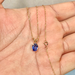 AA oval tanzanite solitaire pendant in 14K yellow gold, showing sculptural four-prong setting, violet color depth, and scale on an 18-inch gold chain. 