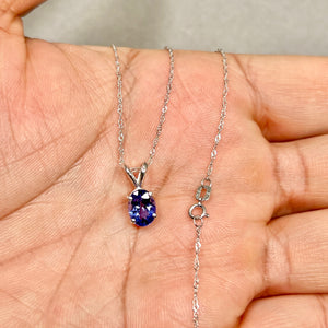 Platinum solitaire pendant featuring an 8x6 mm oval AA tanzanite in a four-prong setting, showing medium violet colour and smooth polished metal, displayed at true pendant scale on an 18 inch white gold chain. 