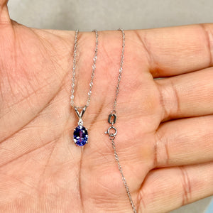 Platinum solitaire pendant featuring an 8x6 mm oval AA tanzanite in medium violet tone, accented by a small round white diamond above the stone, shown on a fine Singapore chain with smooth polished finish and balanced scale. 