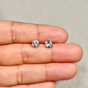Light blue AA aquamarine stud earrings showing 6 mm round stones in polished platinum with visible three-prong sculptural setting for scale reference. 
