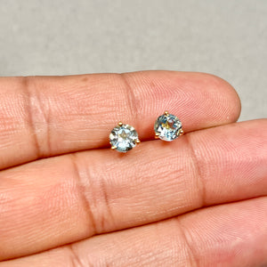 Pair of 6 mm light blue round aquamarine stud earrings in 18K yellow gold, three-prong setting with smooth polished finish 