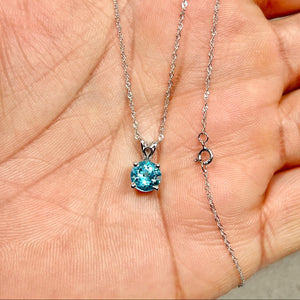 Round Swiss Blue Topaz solitaire pendant in 14K white gold, medium blue 7 mm stone on an 18-inch Singapore chain, showing polished scroll details. 