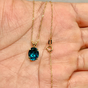 Oval London Blue Topaz pendant in 18K yellow gold, dark blue gemstone in a polished scroll design, shown at close range to highlight surface shine and scale. 