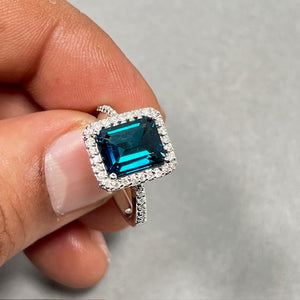 14K white gold women’s fashion ring featuring an emerald-cut London Blue Topaz gemstone measuring 10x8 mm, prong set in a rhodium-finished band. Designed with 38 round white diamonds totaling 0.26 CT, H color and SI clarity, highlighting deep blue and white contrast in a refined 2.5 mm gold setting. 
