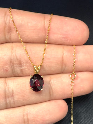 Oval medium red garnet scroll pendant crafted in 14K yellow gold, featuring a natural AAA garnet in prong setting with elegant scroll design, paired with an 18 inch Singapore chain for refined everyday wear. 