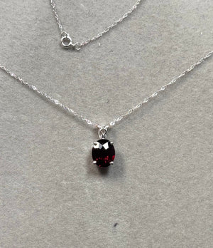 Elegant 14K white gold scroll pendant featuring a natural oval red garnet gemstone weighing 2.90–3.90 carats, AAA quality, prong set with a polished finish, paired with an 18 inch Singapore chain and spring ring clasp. 