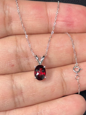 Oval red garnet solitaire pendant for women crafted in 14K white gold, featuring a natural AAA quality garnet weighing 1.35–2.15 carats, prong set in a classic design with an 18 inch white gold Singapore chain and spring ring clasp. 