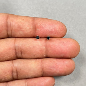 Close-up view of AA quality round black diamond stud earrings set in polished 18K white gold. Each 2.50–3.00 mm black diamond is secured with a classic three-prong setting, offering a clean, minimal profile. Finished with push back closures, these women’s stud earrings present a refined balance of contrast and everyday elegance. 