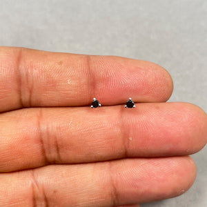 Platinum black diamond stud earrings featuring two AAA quality round black diamonds, 2.50–3.00 mm in size, secured in a classic three prong setting. Elegant 1/9 carat total weight studs with push back closure for women. 