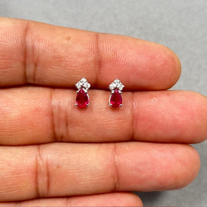 Elegant pear shaped natural ruby and diamond stud earrings in solid 14K white gold, featuring 1.02 Ct total ruby weight and 0.06 Ct round diamonds. Prong set design with secure push backs and rhodium finish, showcasing vibrant red gemstones with brilliant white diamond accents for a refined and timeless look. 