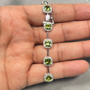 14K white gold bracelet featuring eleven cushion cut natural peridots totaling 10.60 carats, accented by 0.55 carat round diamonds. Prong set gemstones create a vibrant green and white sparkle, secured with a box clasp and safety. Elegant 7.40 inch luxury bracelet for women with fine craftsmanship and refined finish. 
