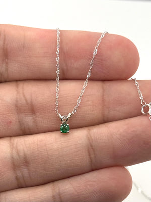 Round green emerald necklace arranged on a neutral background with minimalist white gold styling