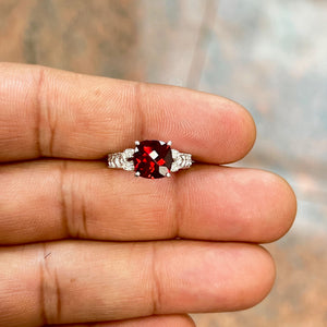 Elegant antique filigree ring crafted in 14K white gold featuring a 2.86 Ct AAA cushion checkerboard garnet with deep red brilliance. Accented by 0.04 Ct round diamonds in a delicate prong setting, this size 3.5 women’s ring showcases intricate vintage-inspired detailing with a refined rhodium finish, blending classic craftsmanship with modern sophistication. 
