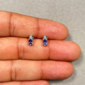 AA natural tanzanite stud earrings in 14K white gold featuring oval 0.54 Ct medium-violet gemstones accented by round white diamonds totaling 0.02 Ct. Prong-set design enhances color depth and brilliance, finished with rhodium plating for a bright surface. Lightweight 0.30-inch earrings with secure push-back closure, offering refined everyday wear with a clean, minimal silhouette. 