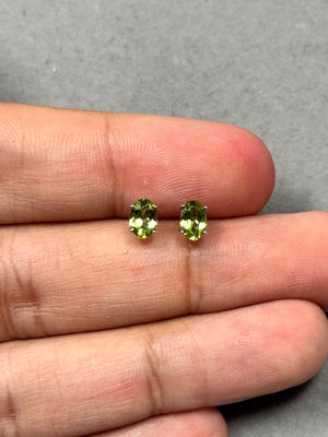 Oval Peridot stud earrings in 14K white gold featuring AAA quality medium-green gemstones in a secure four-prong setting. These elegant 6x4 mm Peridot studs total 0.74 carats and shine with natural brilliance. Designed with rhodium plating and push-back closures, perfect for refined evening style and timeless everyday elegance. 