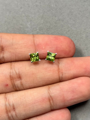 Princess-cut peridot stud earrings in 14K white gold featuring two AAA natural peridots, 5 mm each, in a four-prong setting. These vibrant medium-green gemstone studs offer a fresh pop of colour with a polished rhodium finish and secure push backs for comfortable everyday wear. 