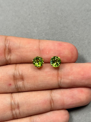 AAA round Peridot stud earrings in 14K yellow gold featuring vibrant medium-green gemstones in a classic four-prong setting. Each stone measures 7 mm with a total weight of 2.77–3.39 carats. Elegant green gemstone studs designed for everyday wear with secure push backs and timeless minimalist style. 