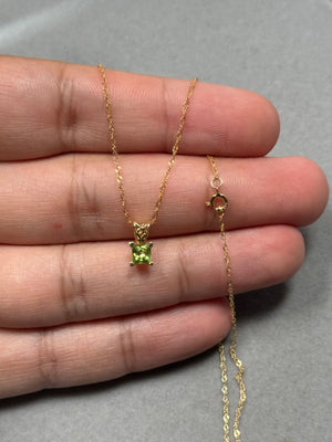 Princess-cut natural peridot scroll pendant in 14K yellow gold, featuring a 0.30–0.40 ct AAA gemstone with vivid green brilliance. Set in an elegant scroll design with secure prongs, this fine women’s necklace hangs from an 18-inch Singapore chain. A delicate yet radiant gold pendant ideal for everyday wear, minimal layering, or refined styling with soft green tones. 