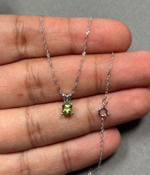 Elegant 0.30–0.40 Ct princess-cut Peridot Scroll Pendant in 14K White Gold, featuring a vivid medium-green AAA-quality gemstone, prong-set for brilliance. Paired with an 18-inch Singapore chain, this delicate pendant offers everyday luxury, soft charm, and refined elegance for women seeking understated, wearable fine jewelry with modern, timeless appeal. 