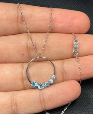 Swiss blue topaz journey circle pendant in 14K white gold featuring five round AA-grade gemstones in a prong-set circular design. Medium-blue stones offer consistent color and brilliance, enhanced by rhodium finish. Suspended from an 18-inch rope chain, this lightweight pendant delivers a clean, modern look ideal for everyday wear and minimalist jewelry styling. 