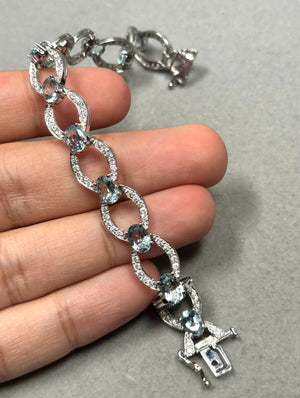 14K white gold aquamarine and diamond bracelet featuring 13 light blue oval aquamarines and 128 round diamonds in prong settings, arranged in a fluid oval link design with rhodium finish, 7 inch length, secured with box clasp and hidden safety, elegant fine jewelry piece with soft blue tones and bright diamond contrast 