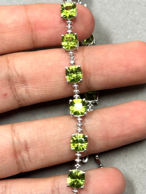 14.54 ct peridot and diamond bracelet in 14K white gold featuring fourteen cushion-cut concave peridots in a vivid medium green tone. The stones are prong-set in a linear design with two accent diamonds, creating a refined and balanced look. Finished with a secure box clasp and hidden safety, this 7-inch bracelet offers a sleek profile suitable for everyday wear. 